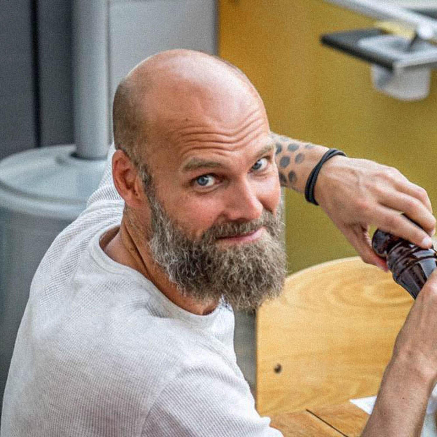 Yoga Kendra Malmö Vinyasa, Hatha, Yin Yoga bald man with a thick, grey-speckled beard looking back over his shoulder toward the camera.