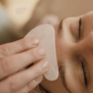 Yoga Kendra Malmö Holistisk Lifting Massage close-up of a person receiving a facial massage treatment using a smooth, pinkish stone tool on their cheek and under-eye area