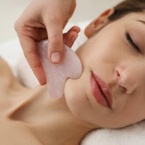 Yoga Kendra Malmö Gua Sha Ansikte woman receiving a facial massage treatment on her jawline using a pink quartz Gua Sha tool