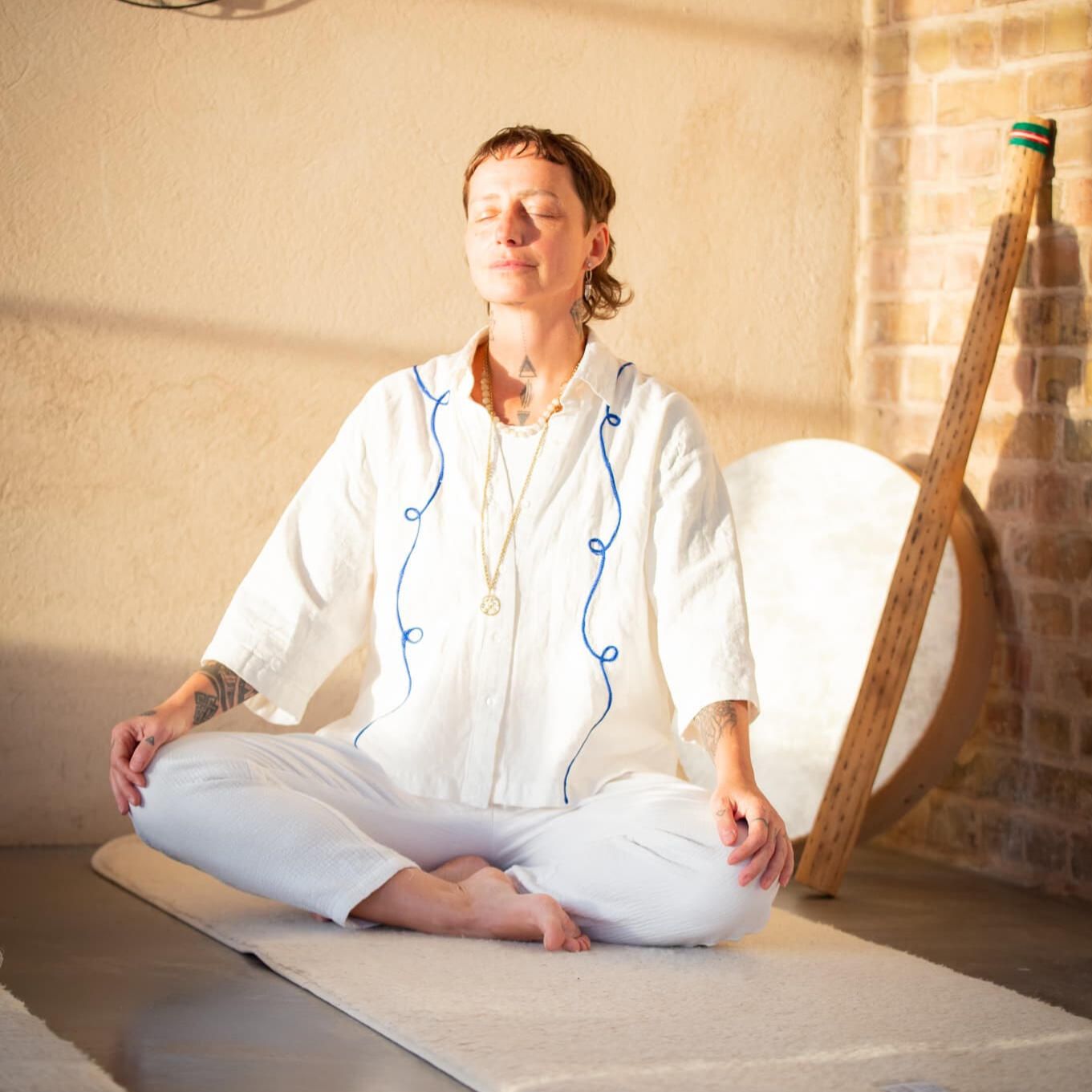 Yoga Kendra Malmö Yin Yoga, Fascia Release, Meditation, Transformational Breathwork, Sound Healing, Deep Therapeutic Bodywork a person sitting cross-legged on a mat with closed eyes, meditating in front of a warm-toned wall.