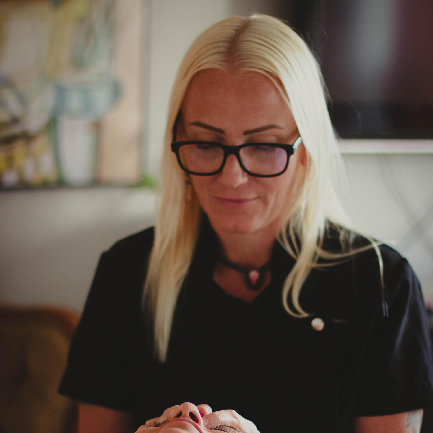 Yoga Kendra Malmö Swedish Medical Massage, Thai Yoga Massage, Lymphatic Massage, Reiki Healing, Cupping Therapy, Nutritional Cou Blonde woman with black framed glasses and black top giving a facial treatment to salon client
