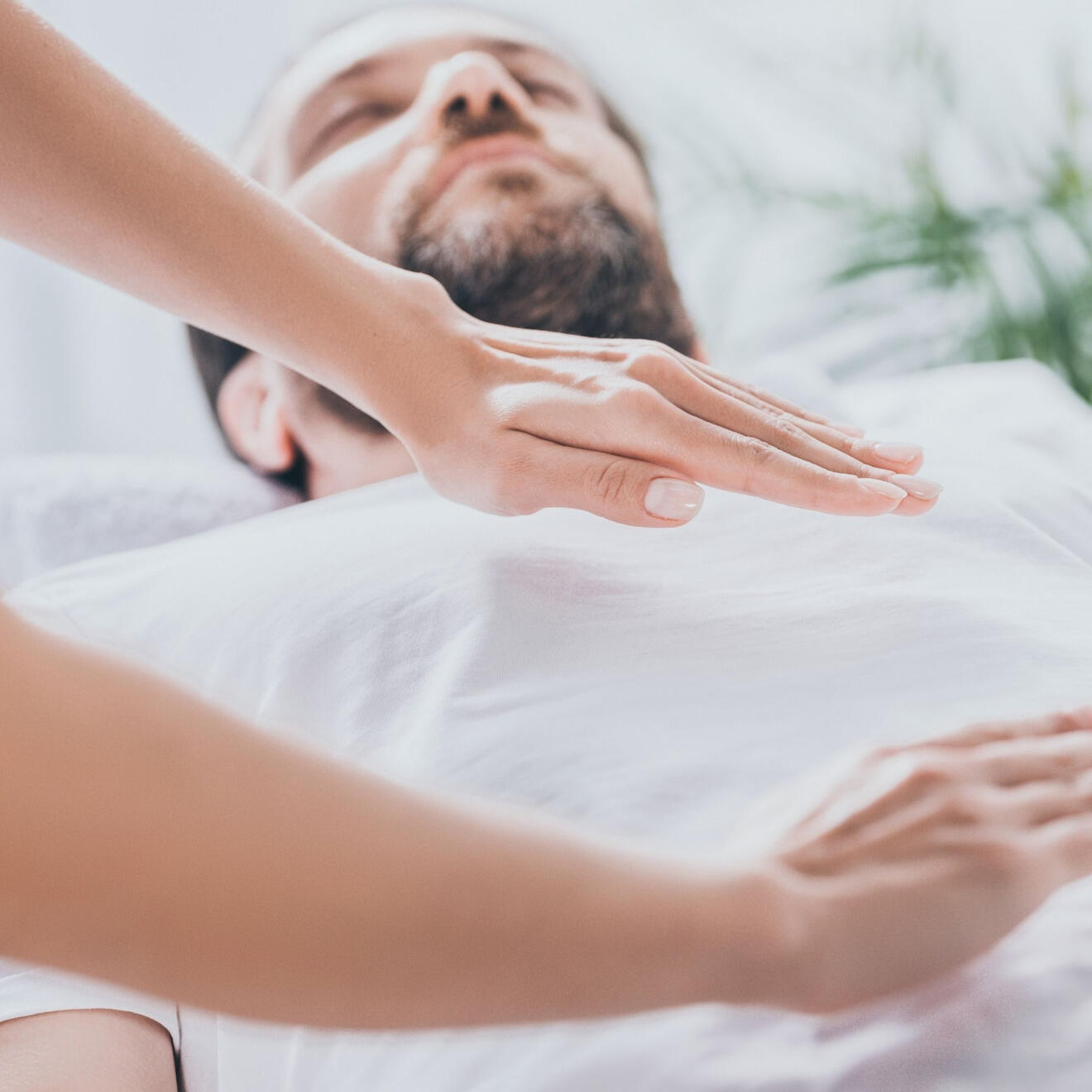 Yoga Kendra Malmö Reiki Healing Man laying on hos back in a white t-shirt receiving reiki healing treatment where the practitioner's hands hover above his chest